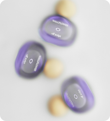 Three purple perfume bottles with beige spheres arranged on a soft, blurred white background.