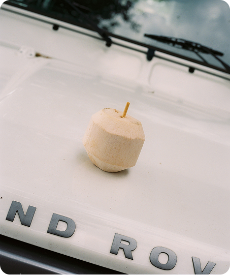 A small carved wooden toy or figurine with a wooden stick inserted at the top, placed on the hood of a white vehicle. 